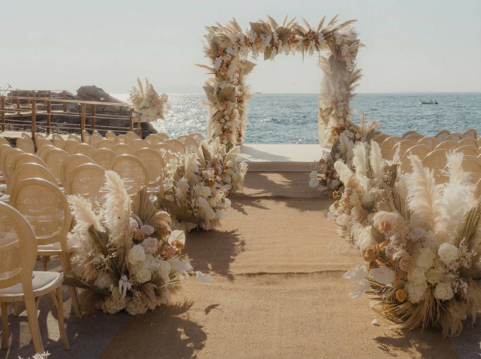 Wedding ceremony setup on a beach with chairs and a floral arch overlooking the sea.