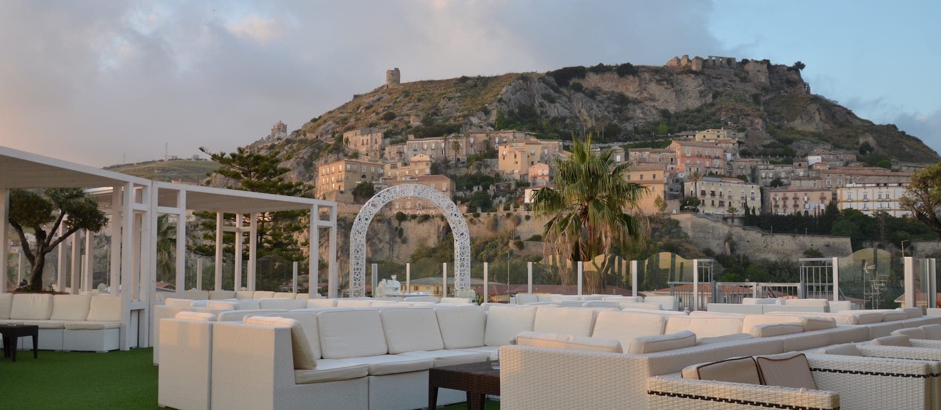 Terrace with white seating and wedding arch overlooking a town on a hill.