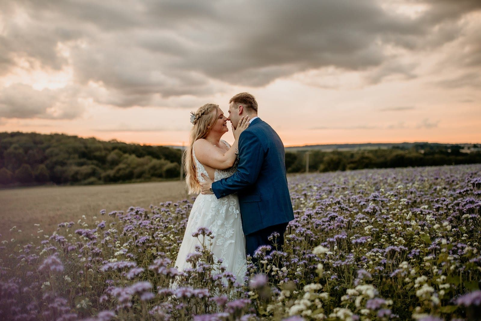 Couple embracing in a field of purple flowers at sunset.