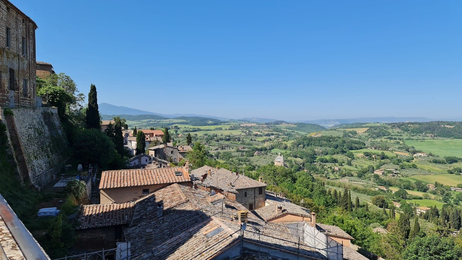 View of rolling green hills and rooftops under a clear blue sky.