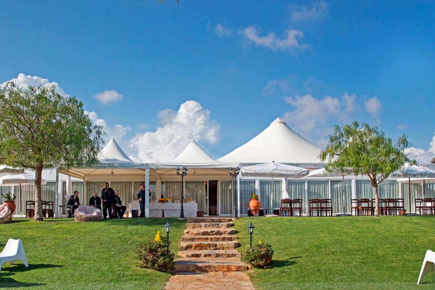 Exterior of a wedding venue with a large white tent and outdoor seating on a sunny day.