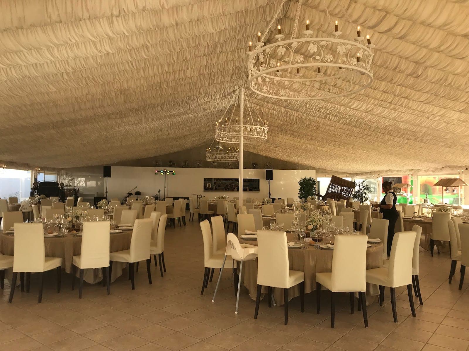 A wedding reception hall with round tables set for guests under a draped ceiling.