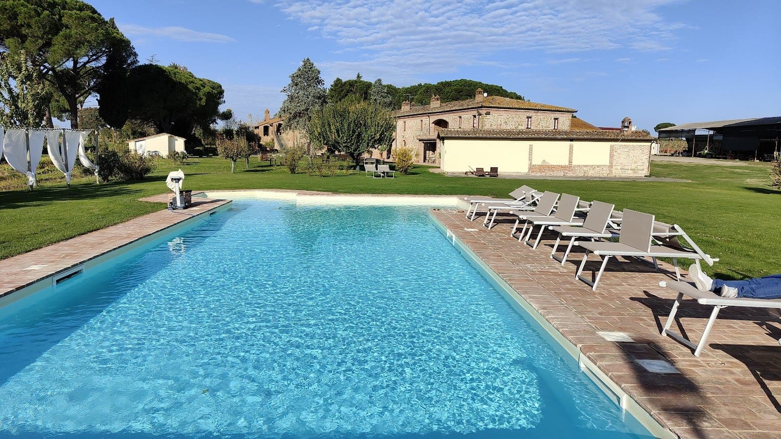 A swimming pool with lounge chairs on the side, with a building and trees in the background.
