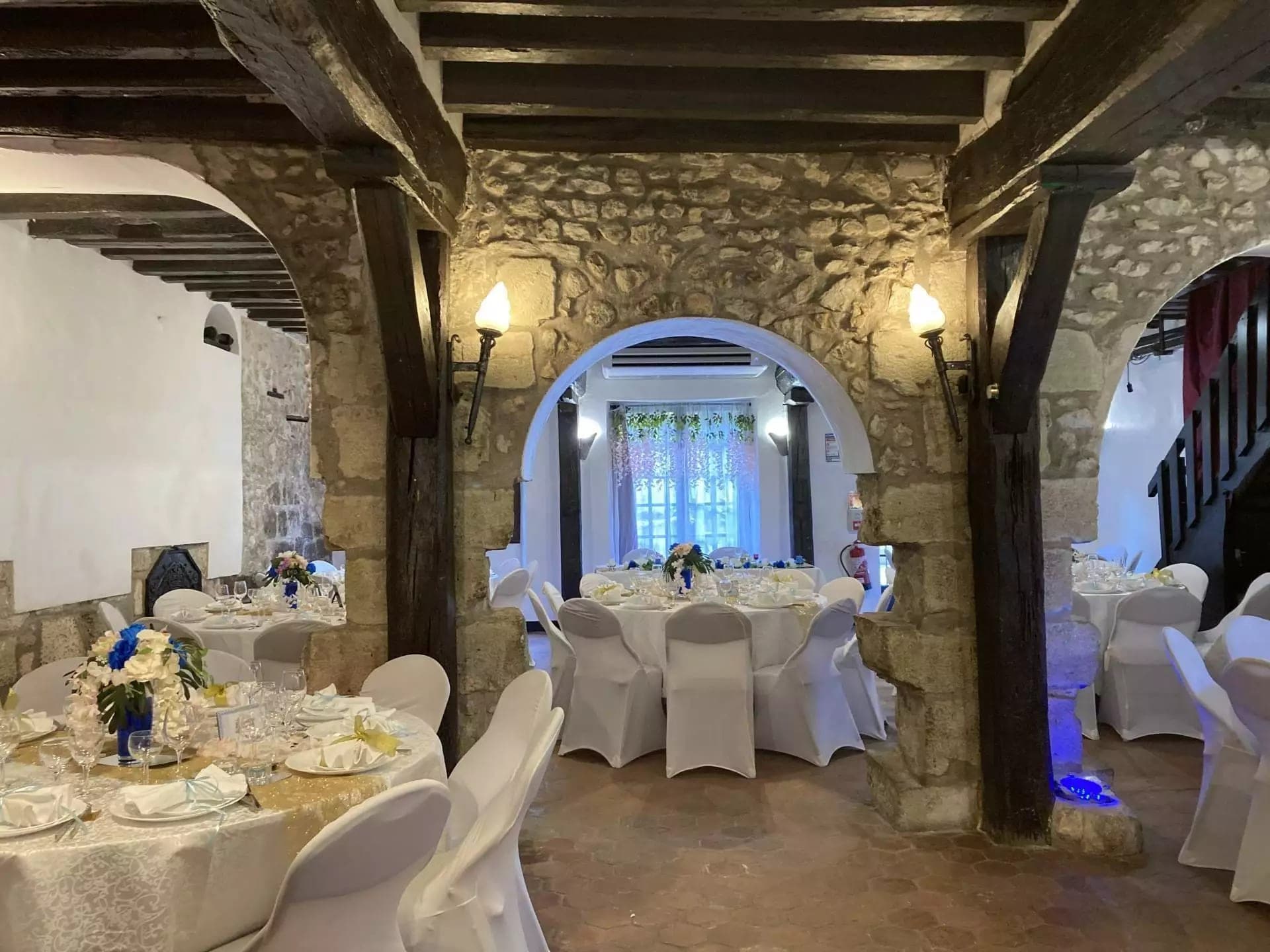 A reception room with round tables set for a wedding, featuring stone walls and wooden beams.