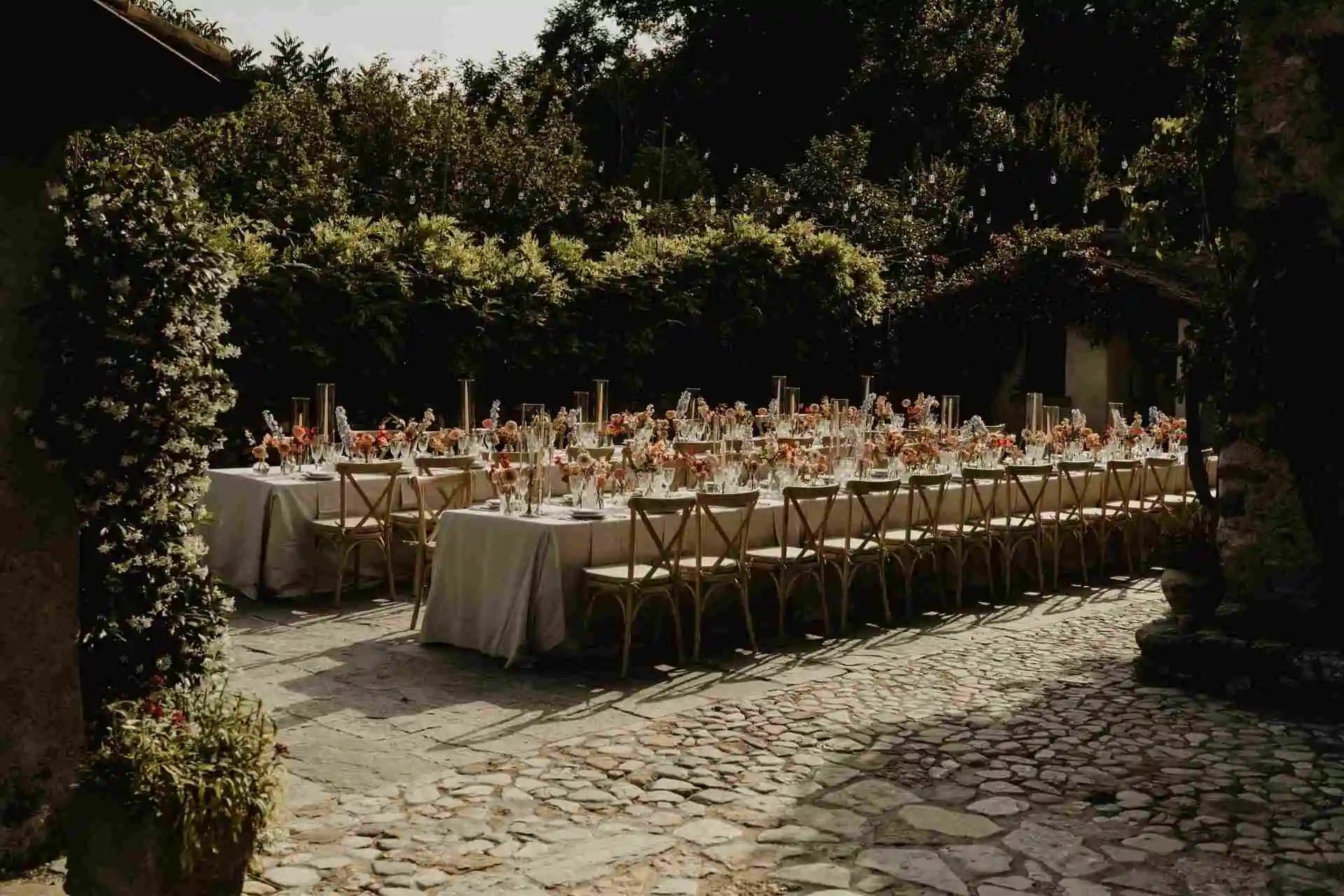 Outdoor reception table setting with chairs and floral arrangements.