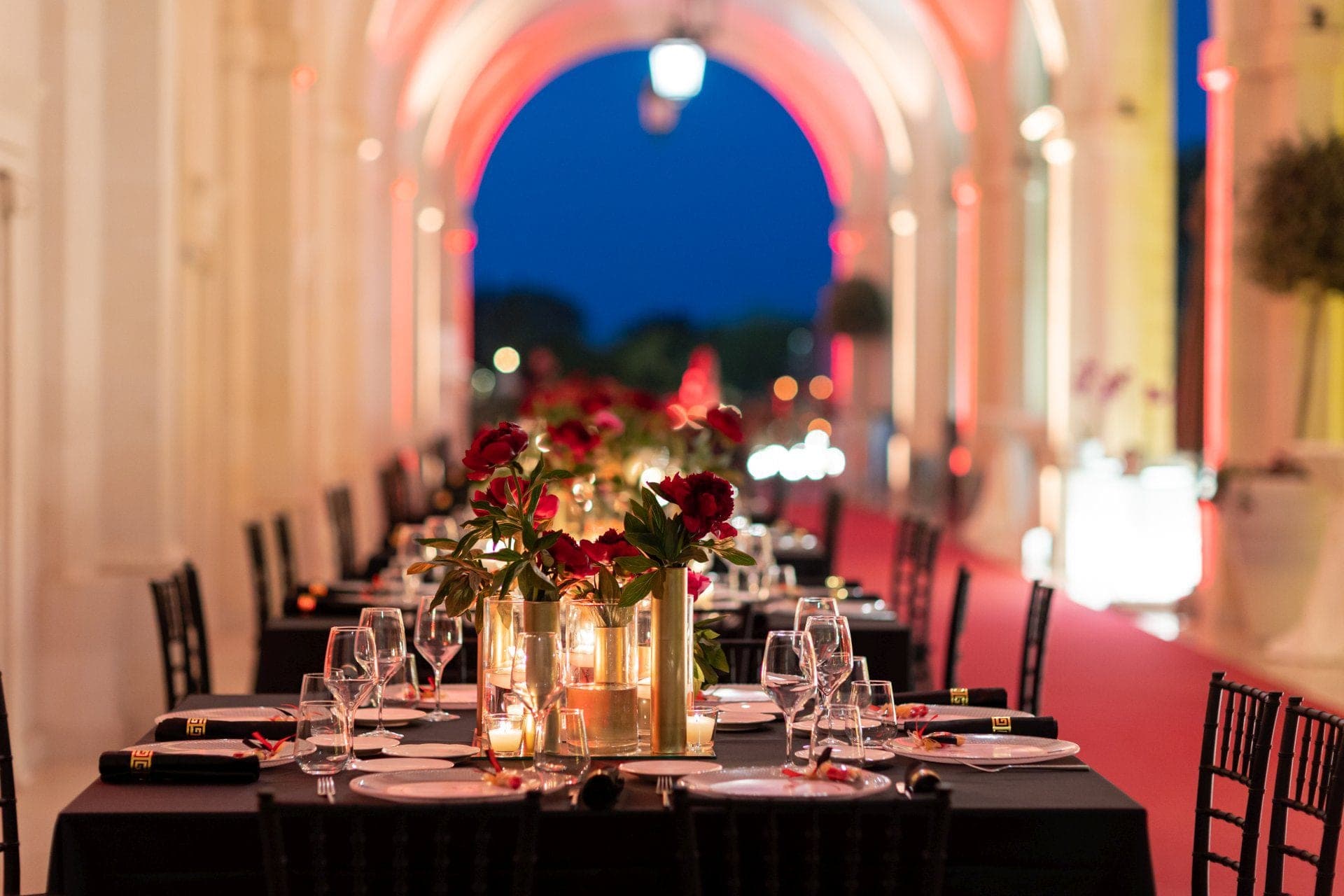 A long table is set for a reception dinner under an illuminated arched walkway.