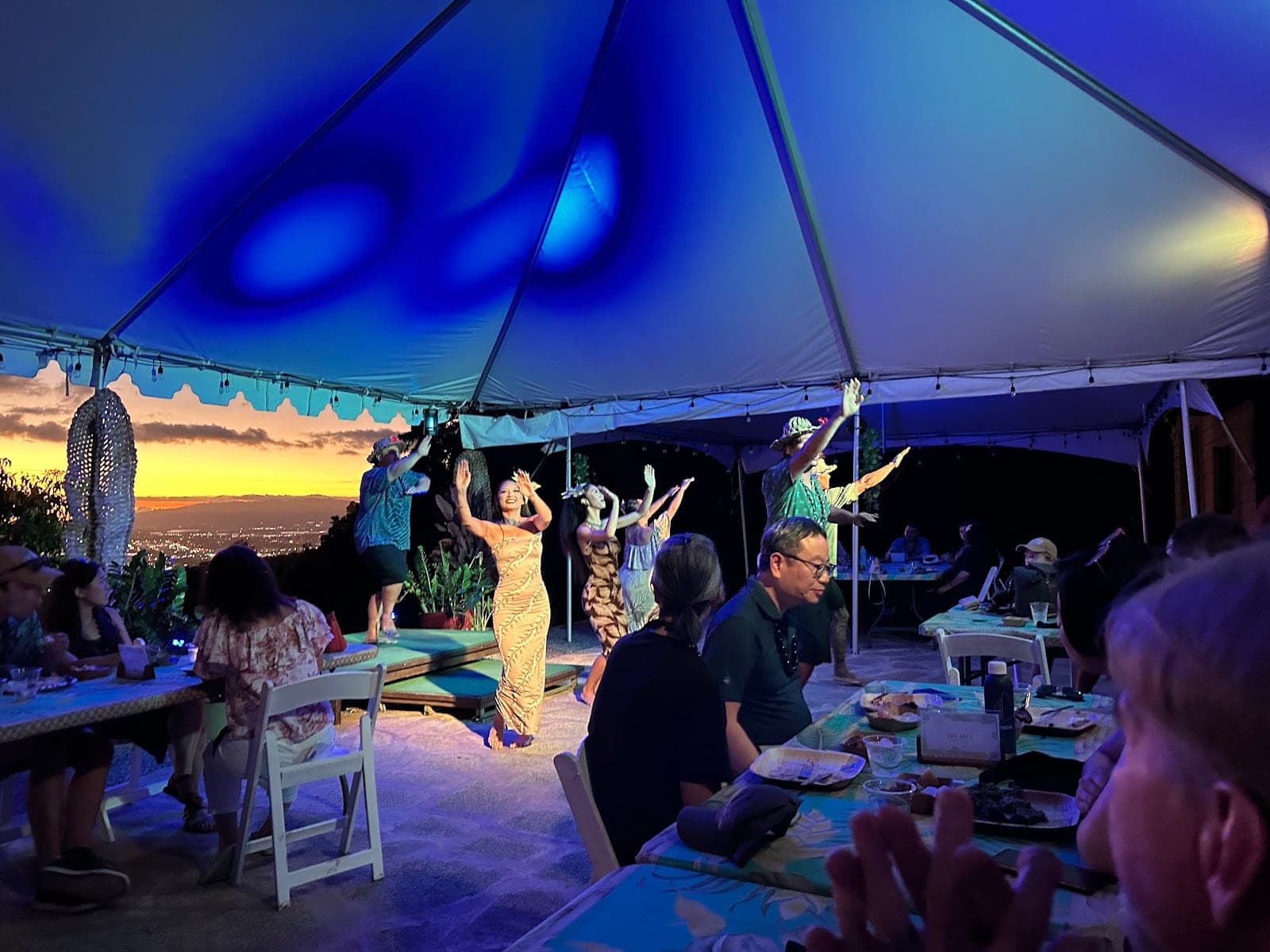 A reception dinner is held under a tent with dancers performing at sunset.