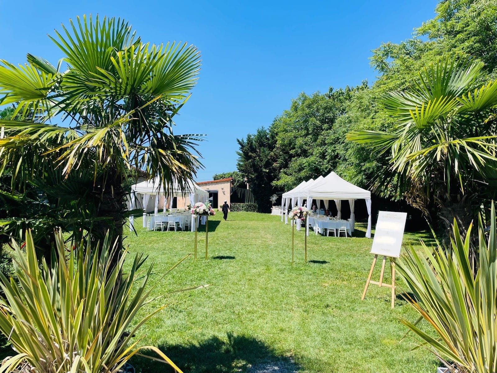 A garden with marquees and tables set up for an event under a clear blue sky.