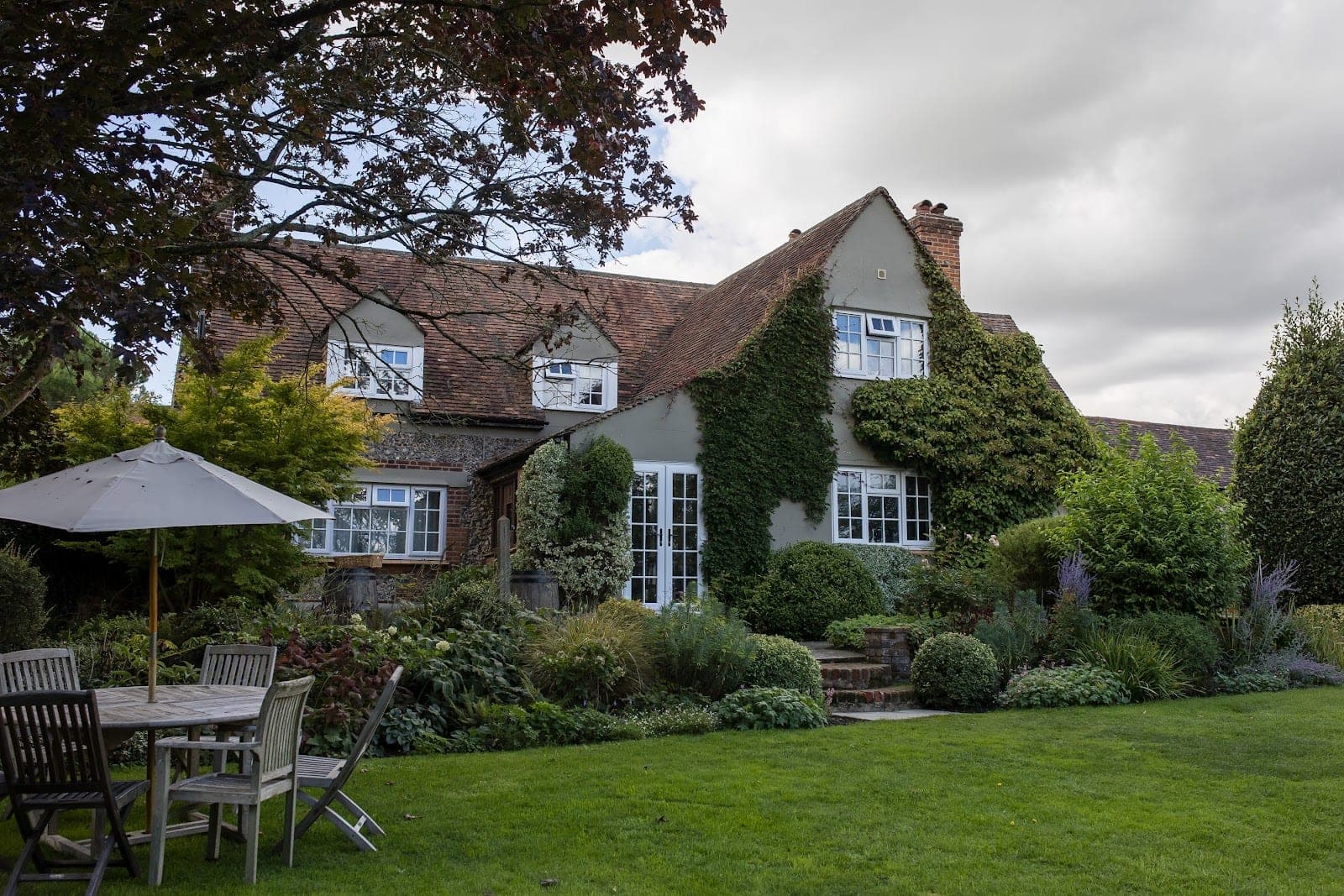 Exterior of a house with ivy, surrounded by a garden and lawn.