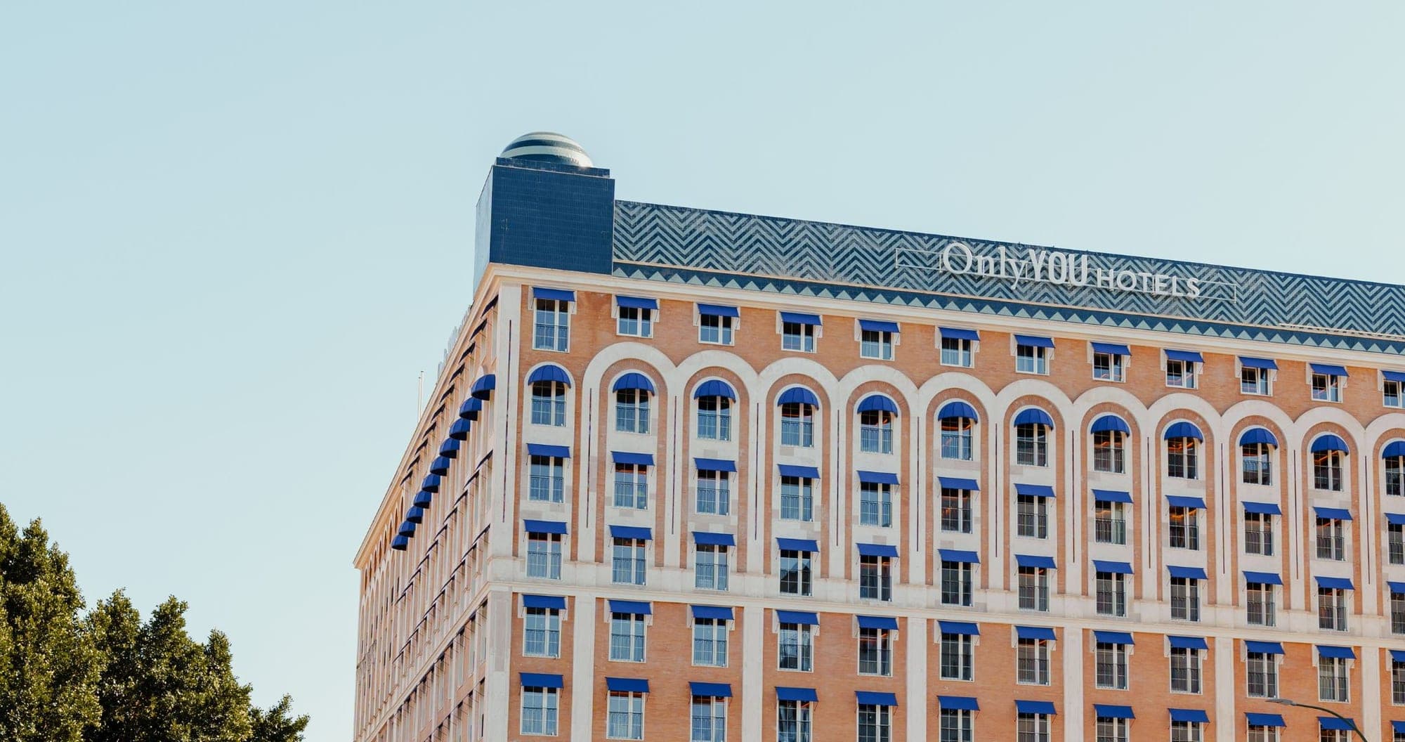 Exterior of a large brick hotel building with blue awnings and a decorative roofline.
