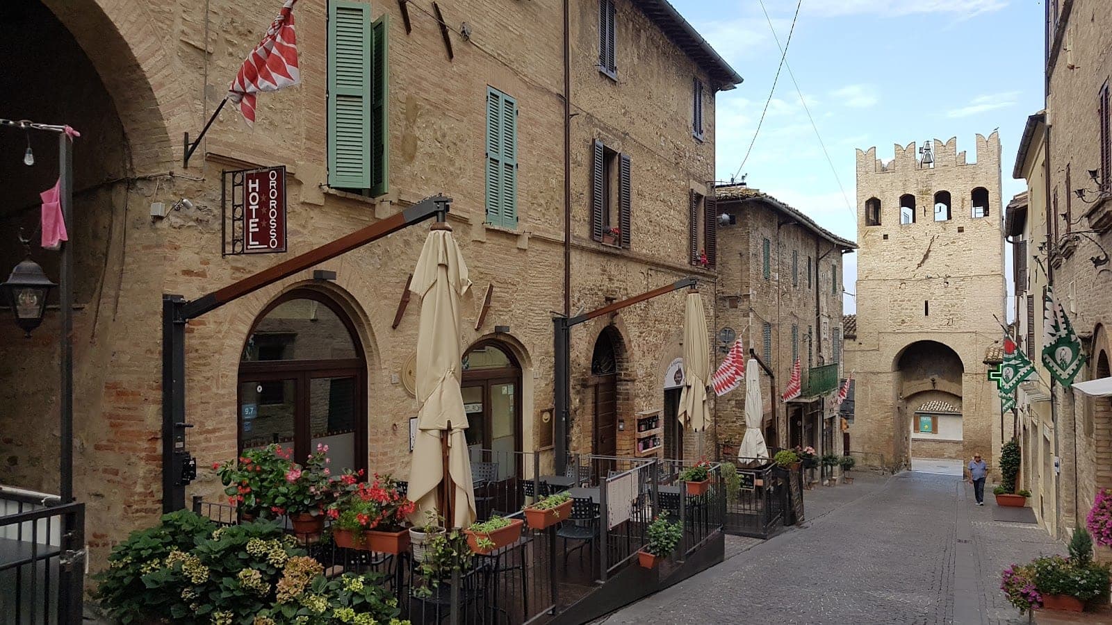 Street view of a hotel and restaurant with outdoor seating and flags.