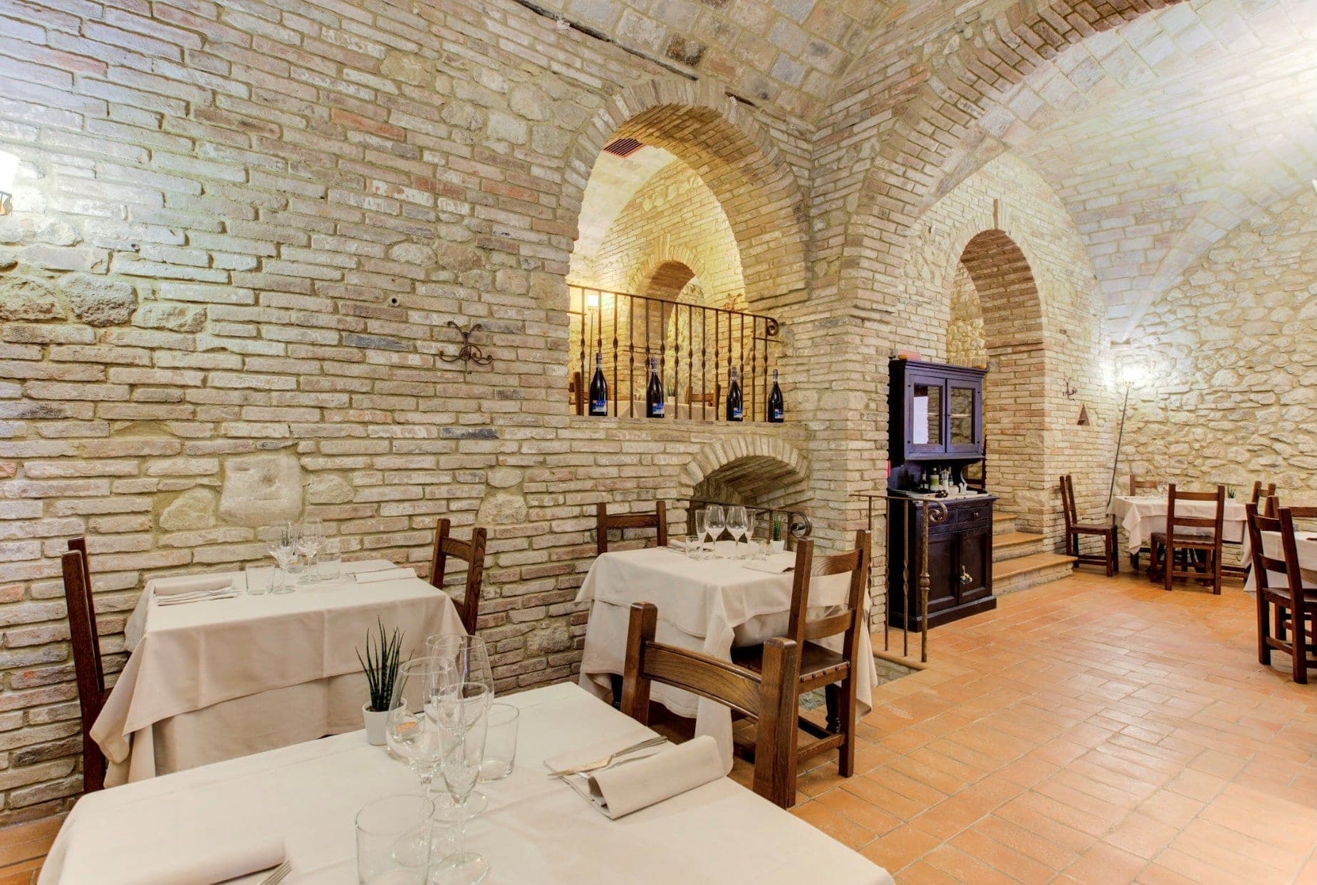A rustic dining room with brick walls, arched ceilings, and tables set for a meal.