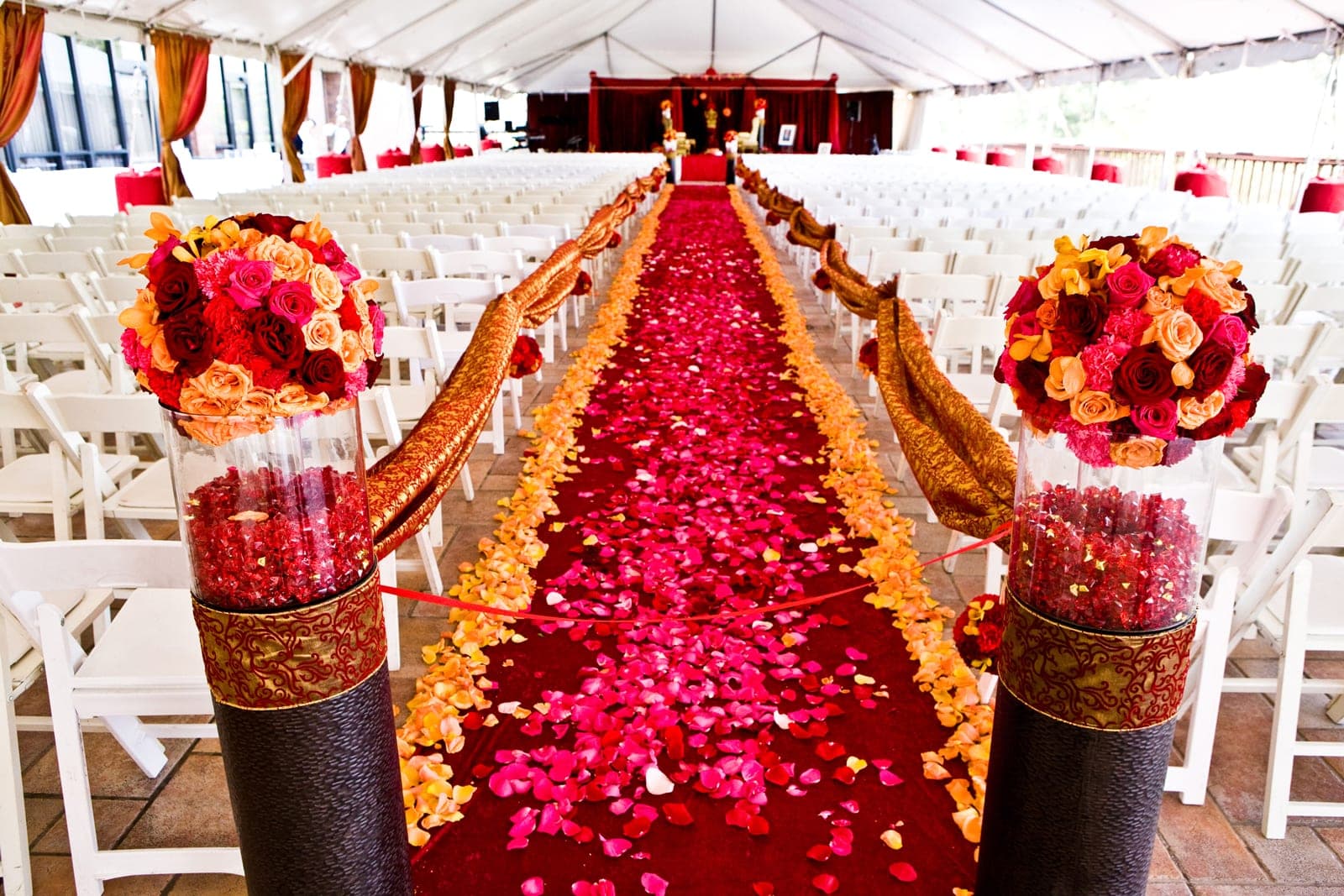 Wedding ceremony setup with a red carpet aisle and white chairs under a tent.