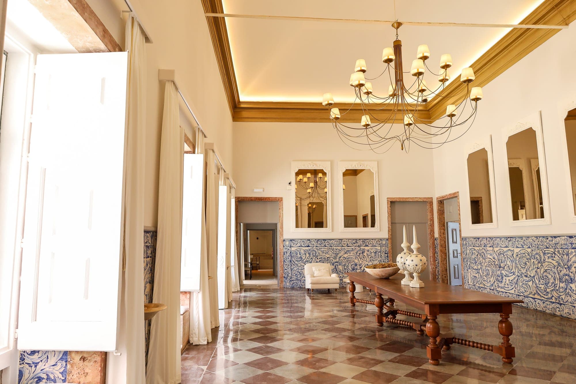 A long wooden table with decorative items in a hall with tiled walls and a checkered floor.