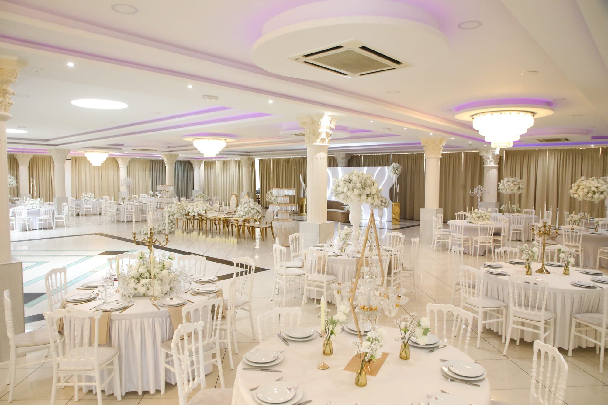 A wedding reception hall with round tables and white chairs.