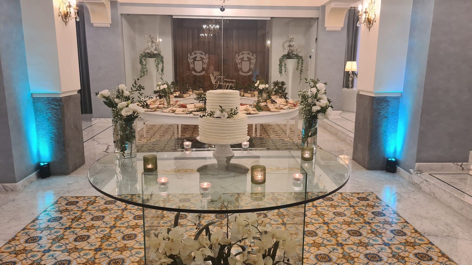 Wedding cake and buffet table with floral arrangements in a venue reception area.