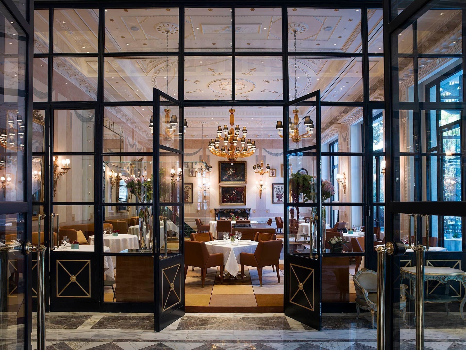 A view through glass doors into a formal dining room with tables set for a meal.