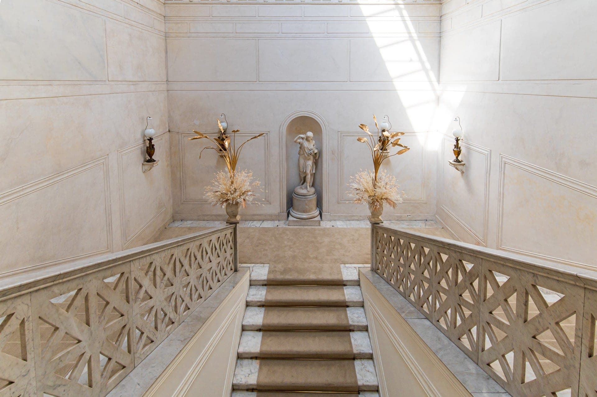 Grand marble staircase with a statue and floral arrangements.