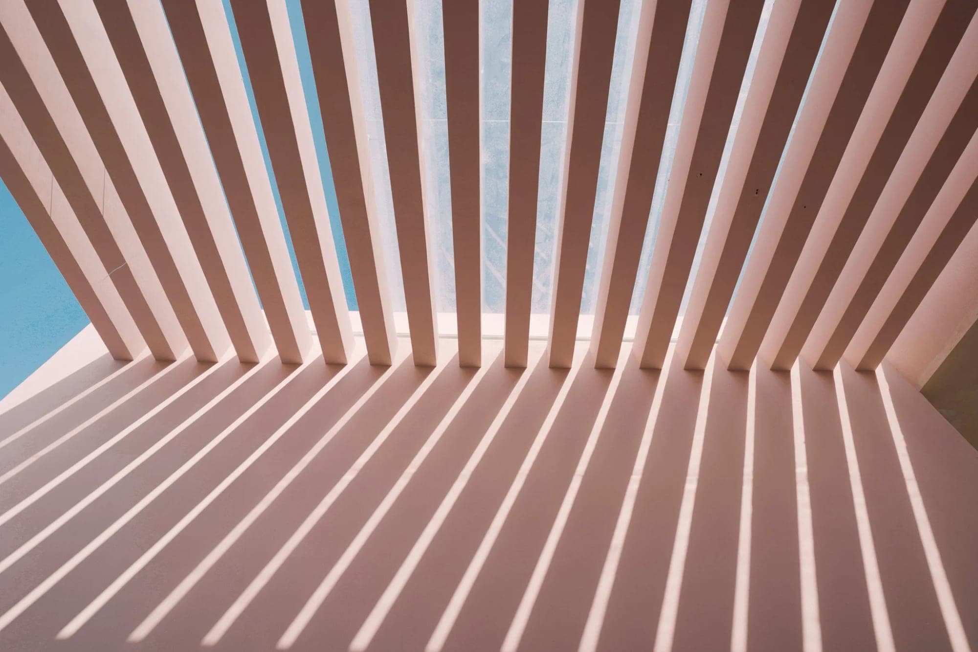Pink pergola with diagonal slats casting shadows on a wall.