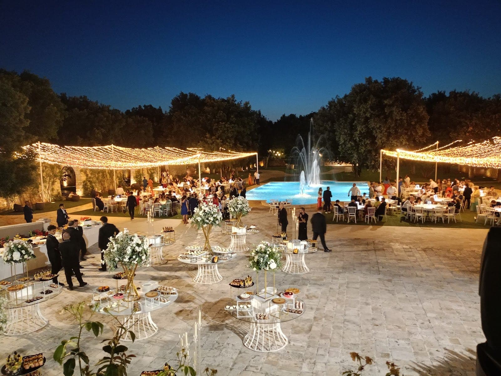 Outdoor reception area with tables, lights, and a fountain at night.