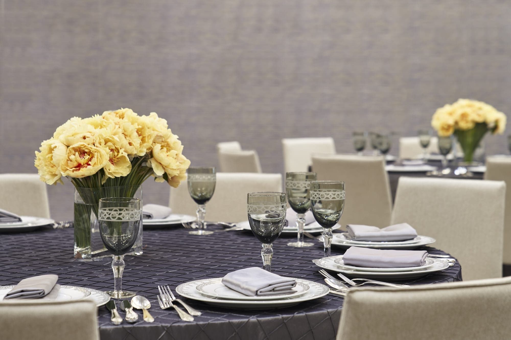 A round reception table is set with plates, cutlery, glasses, and a yellow floral centerpiece.