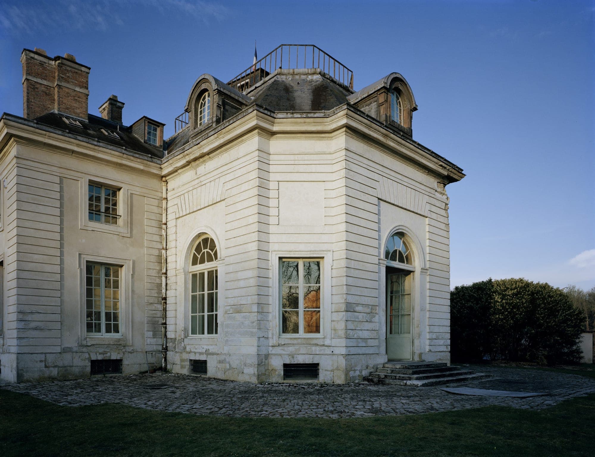 Exterior of a pale stone building with arched windows and a pitched roof.