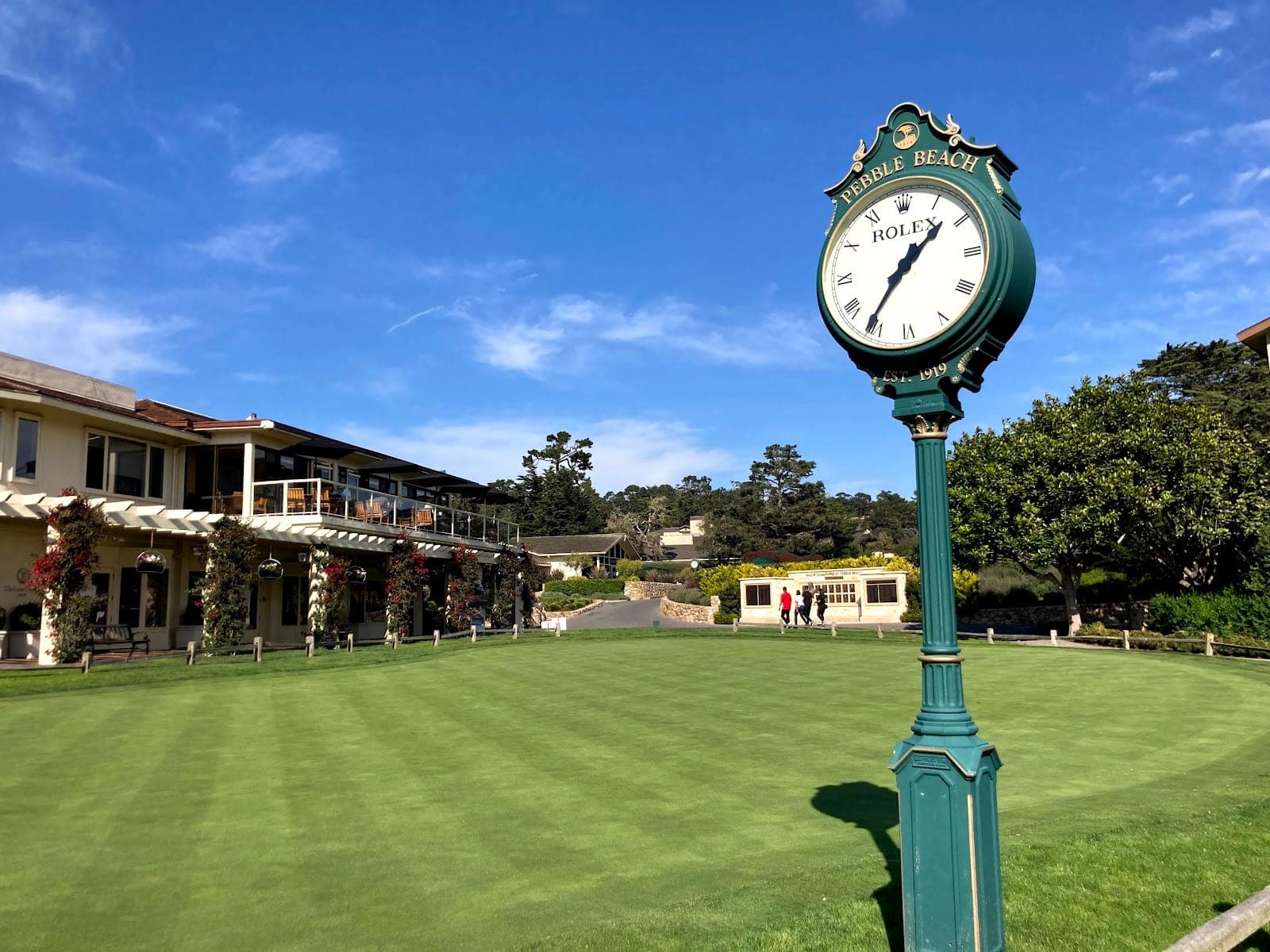 A green clock tower stands on a manicured lawn in front of a building.