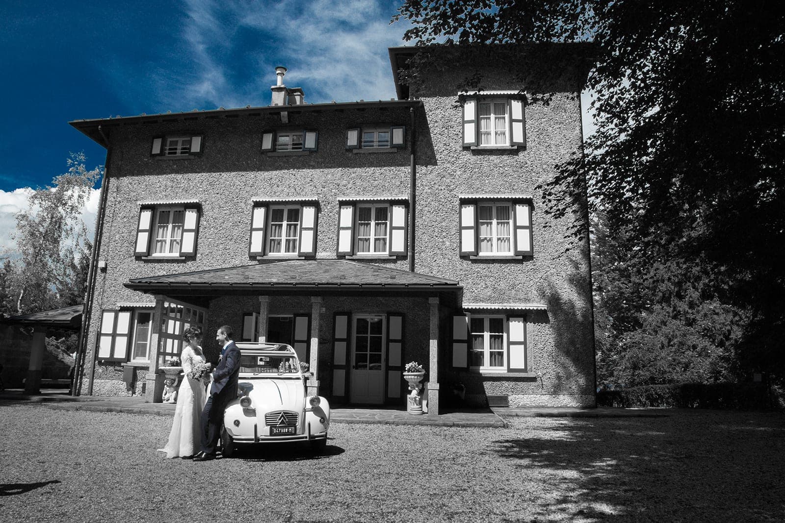 A couple stands by a vintage car in front of a building.