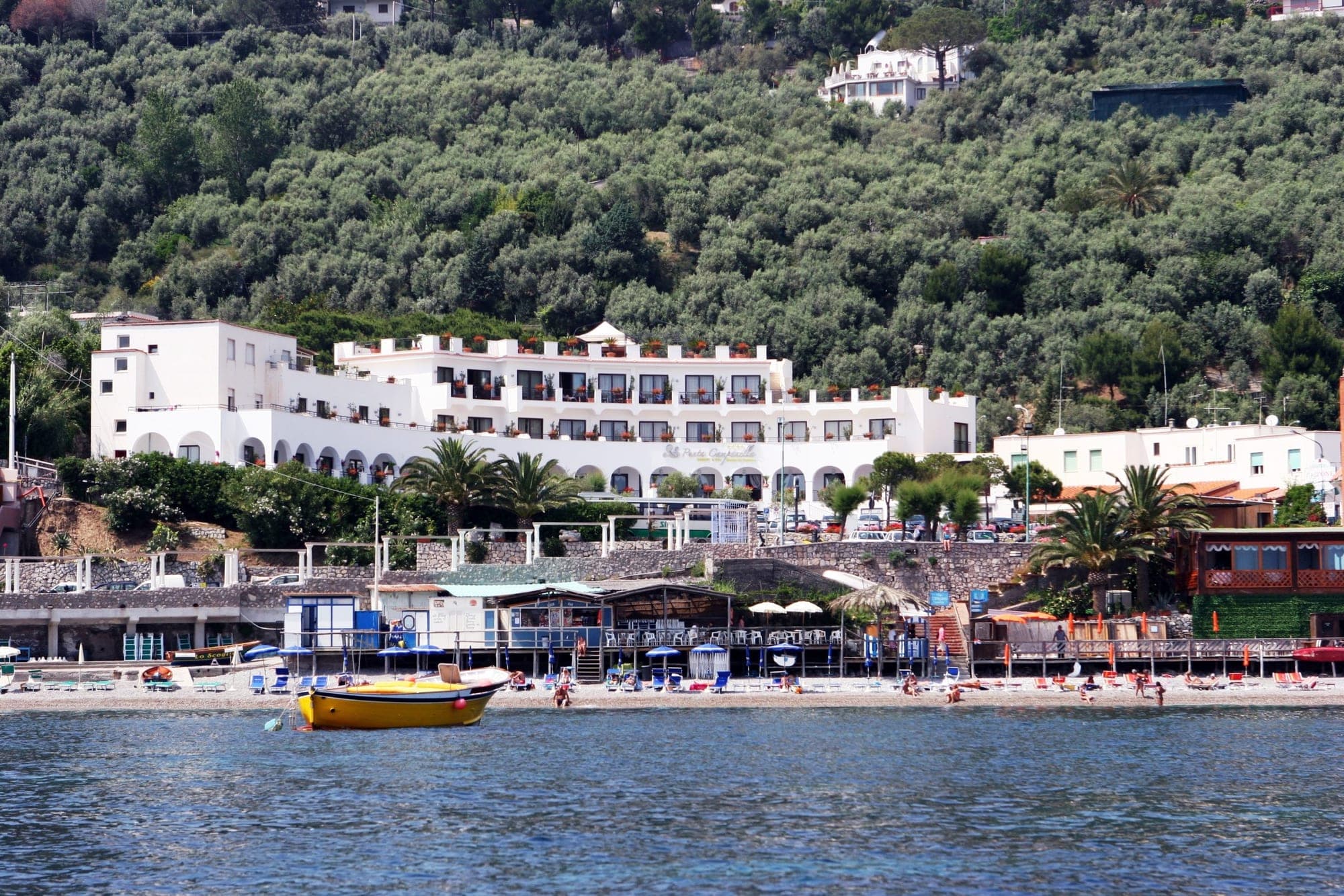 White hotel building on a hillside overlooking a beach and the sea.