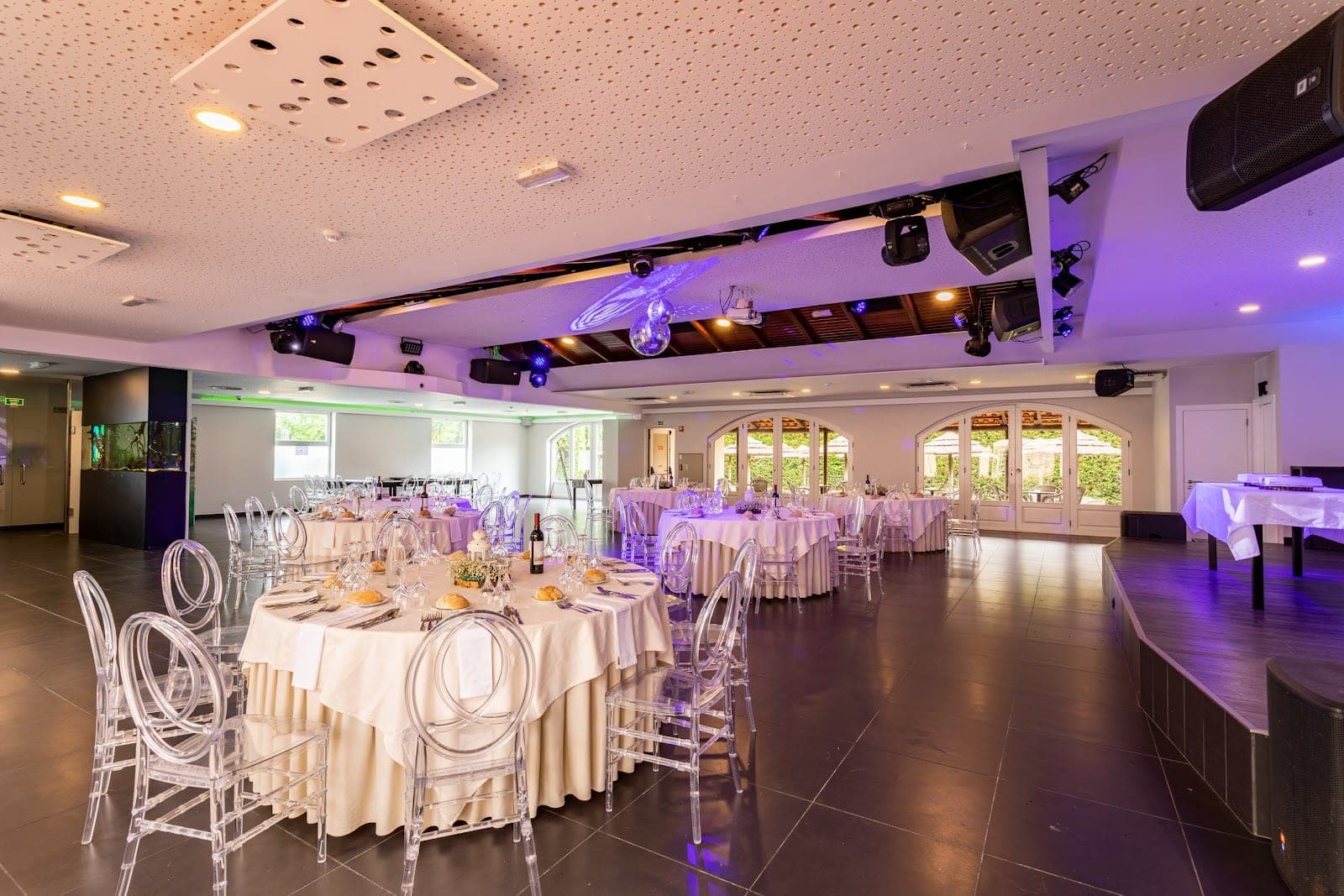 Reception room with round tables set for a wedding and clear chairs.