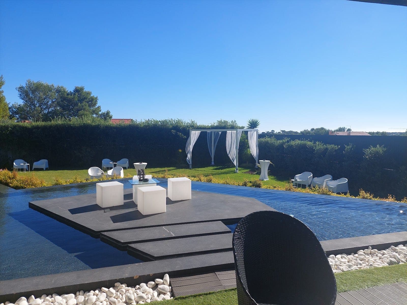 Wedding ceremony setup by a pool with white drapes and seating.