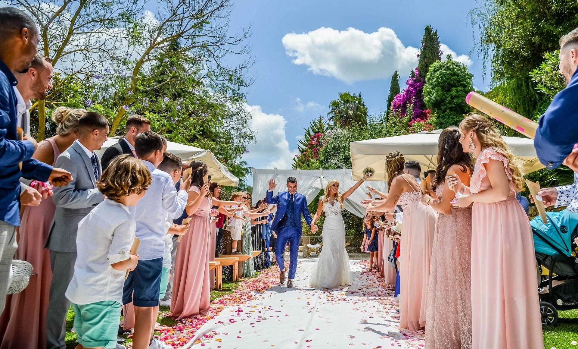 Bride and groom walk down a petal-strewn aisle as guests cheer.