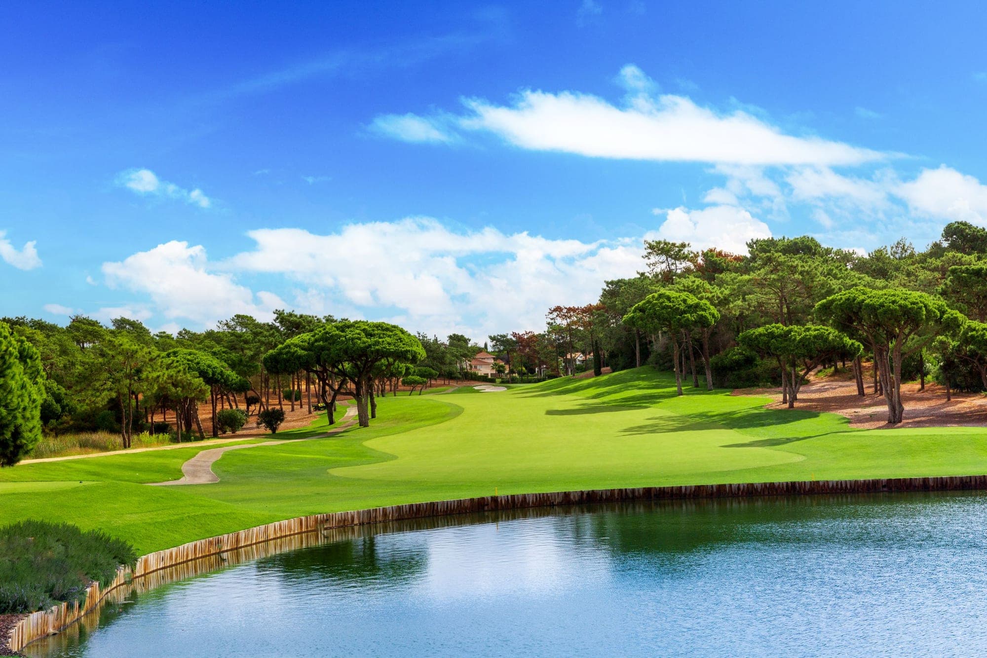 A golf course with a lake and trees under a blue sky with clouds.