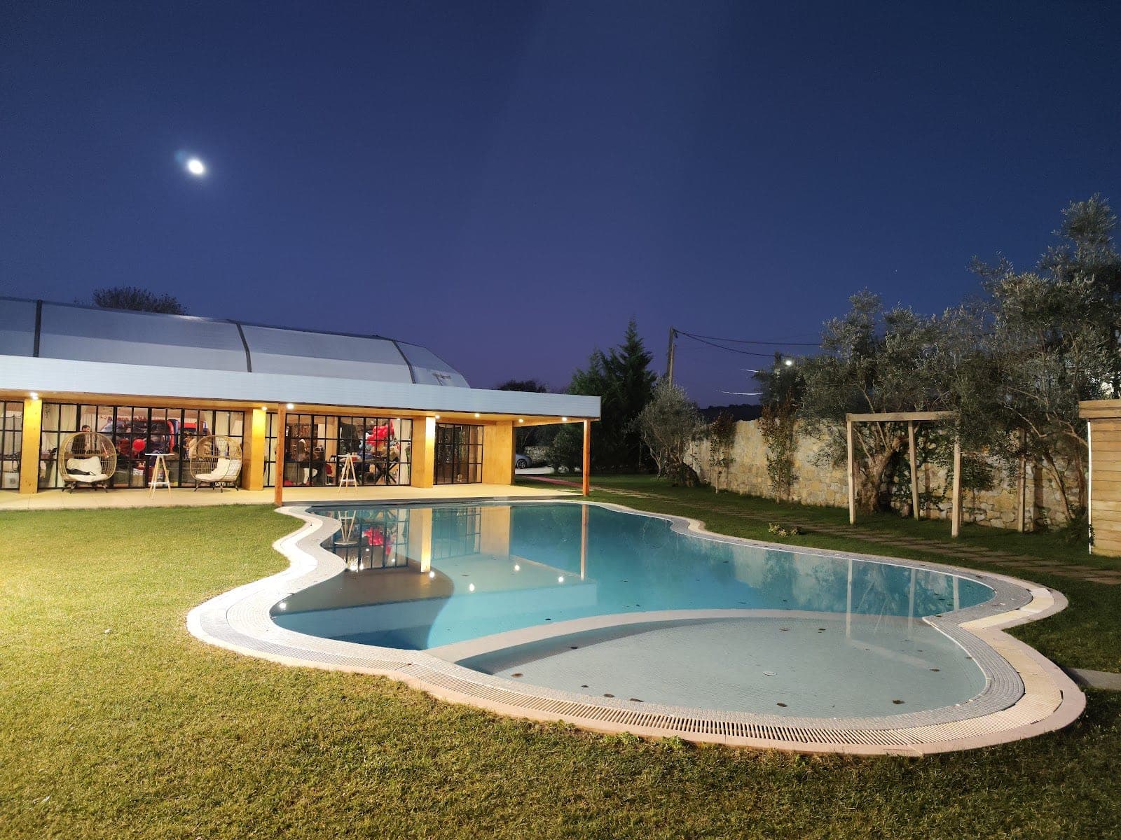 A swimming pool and building at dusk with a moon in the sky.
