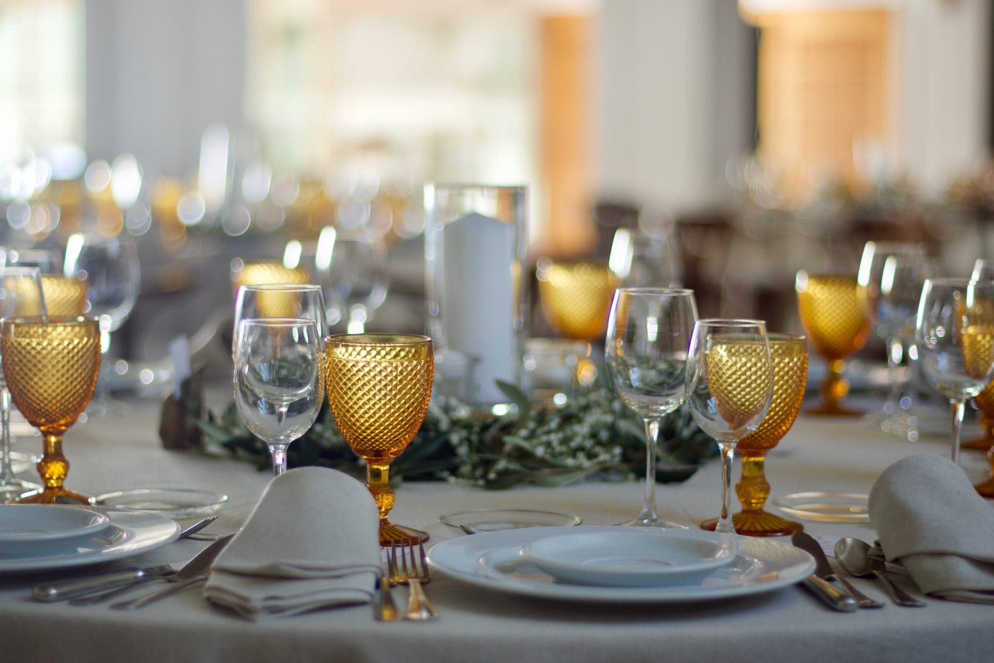 A table is set for a wedding reception with gold goblets and white plates.