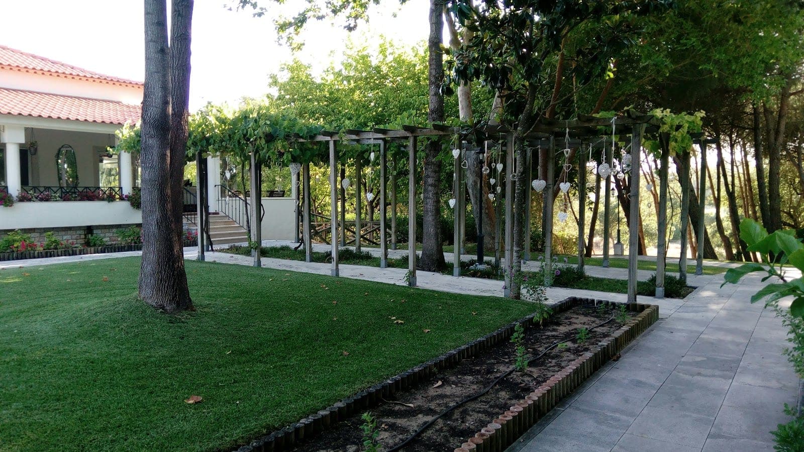 Garden path with pergola and hanging hearts next to a building.