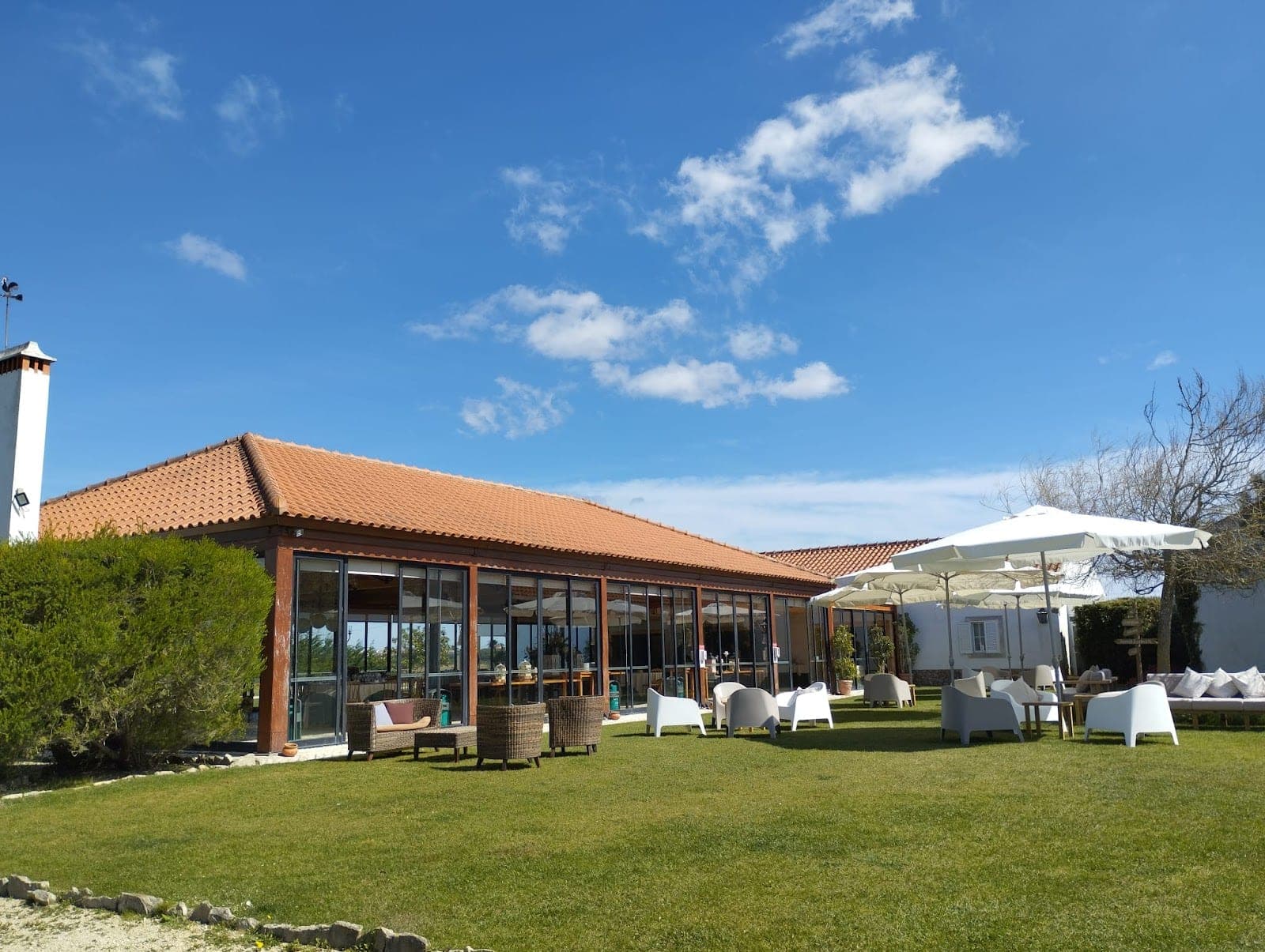 Exterior of a wedding venue with a tiled roof and large windows, set in a green lawn with outdoor furniture.