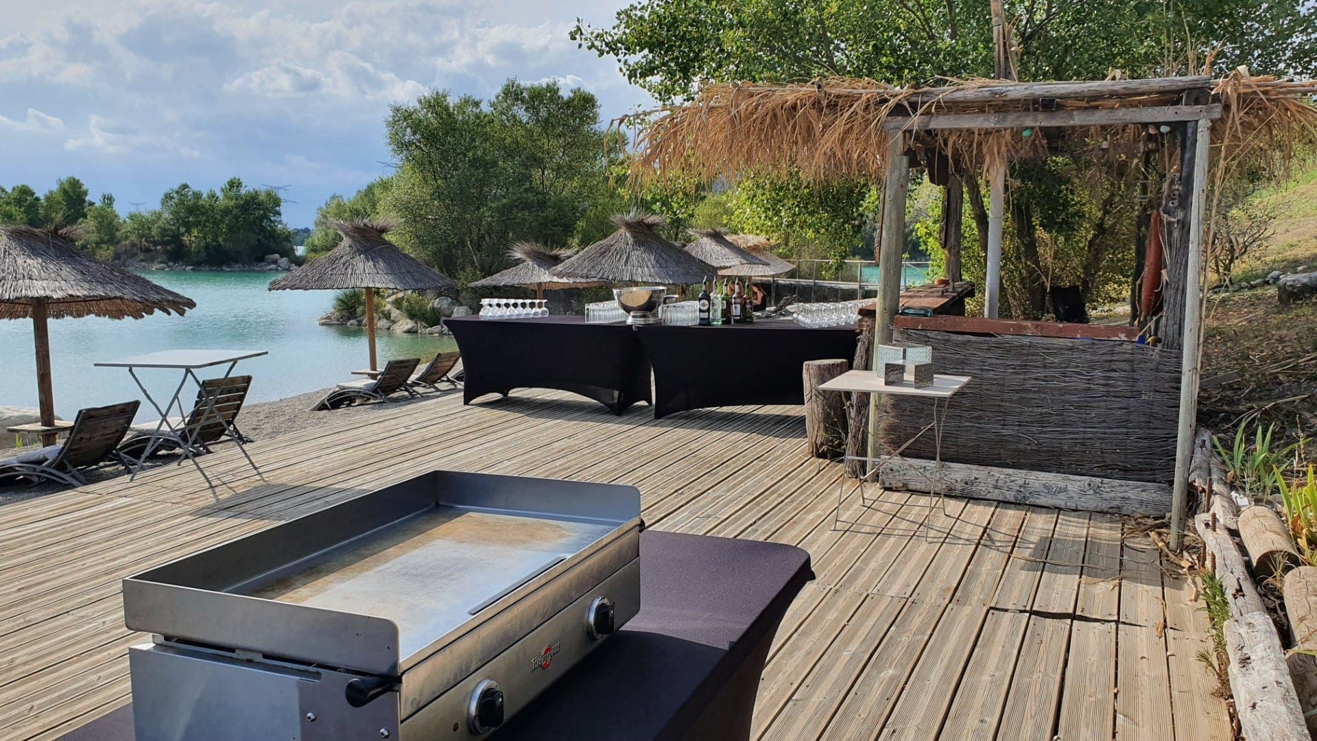Lakeside bar area with thatched umbrellas, lounge chairs, and a griddle.