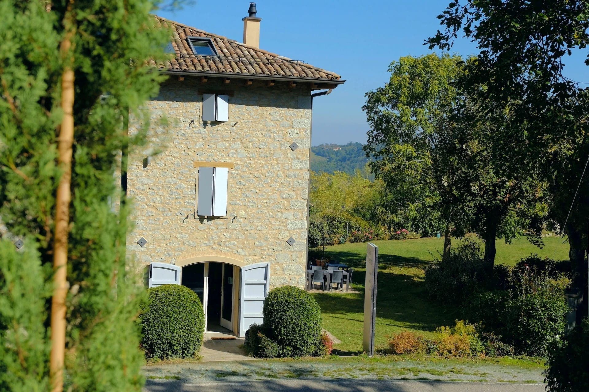 Stone building with blue shutters and a garden on a sunny day.
