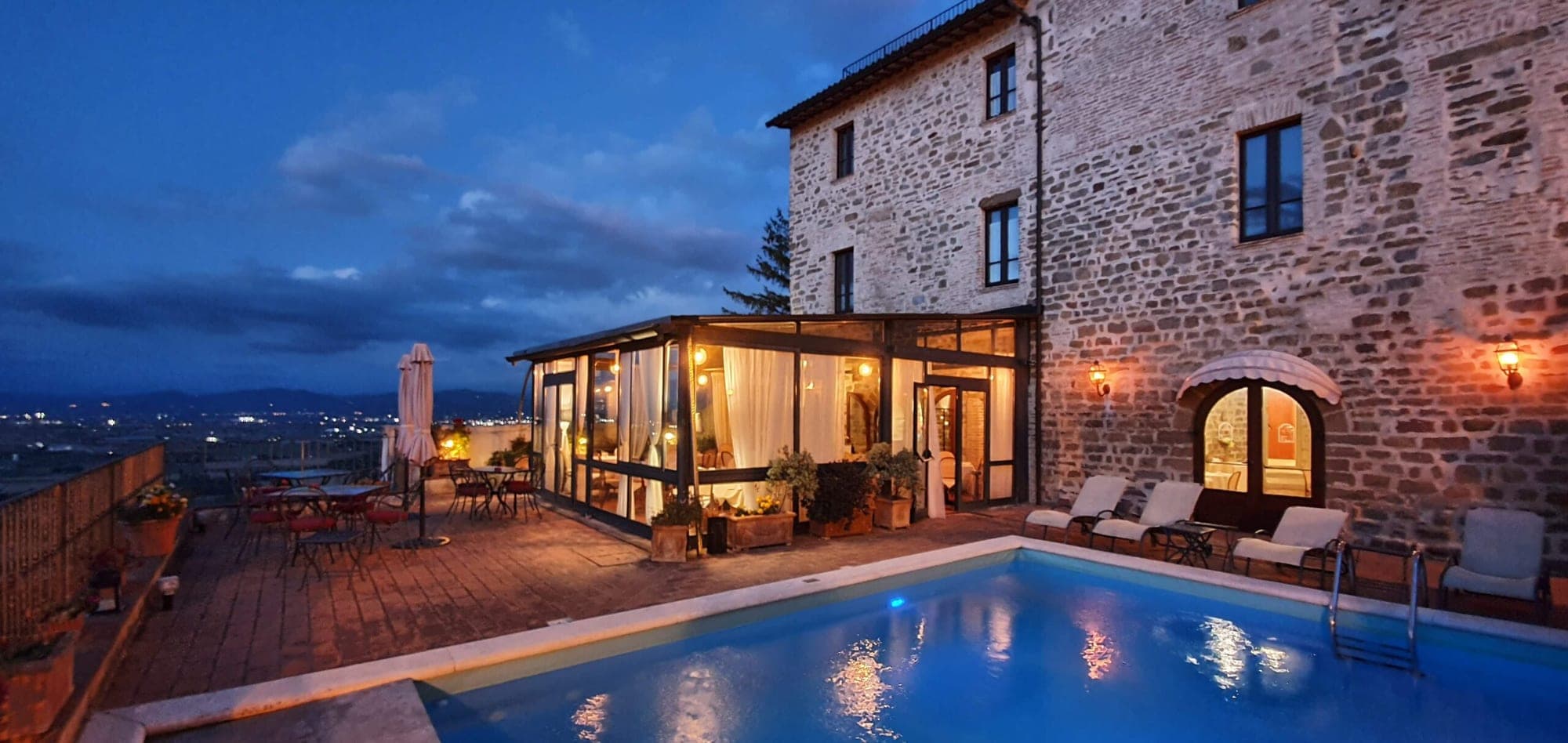 Exterior of a stone building with a pool and seating area at dusk.