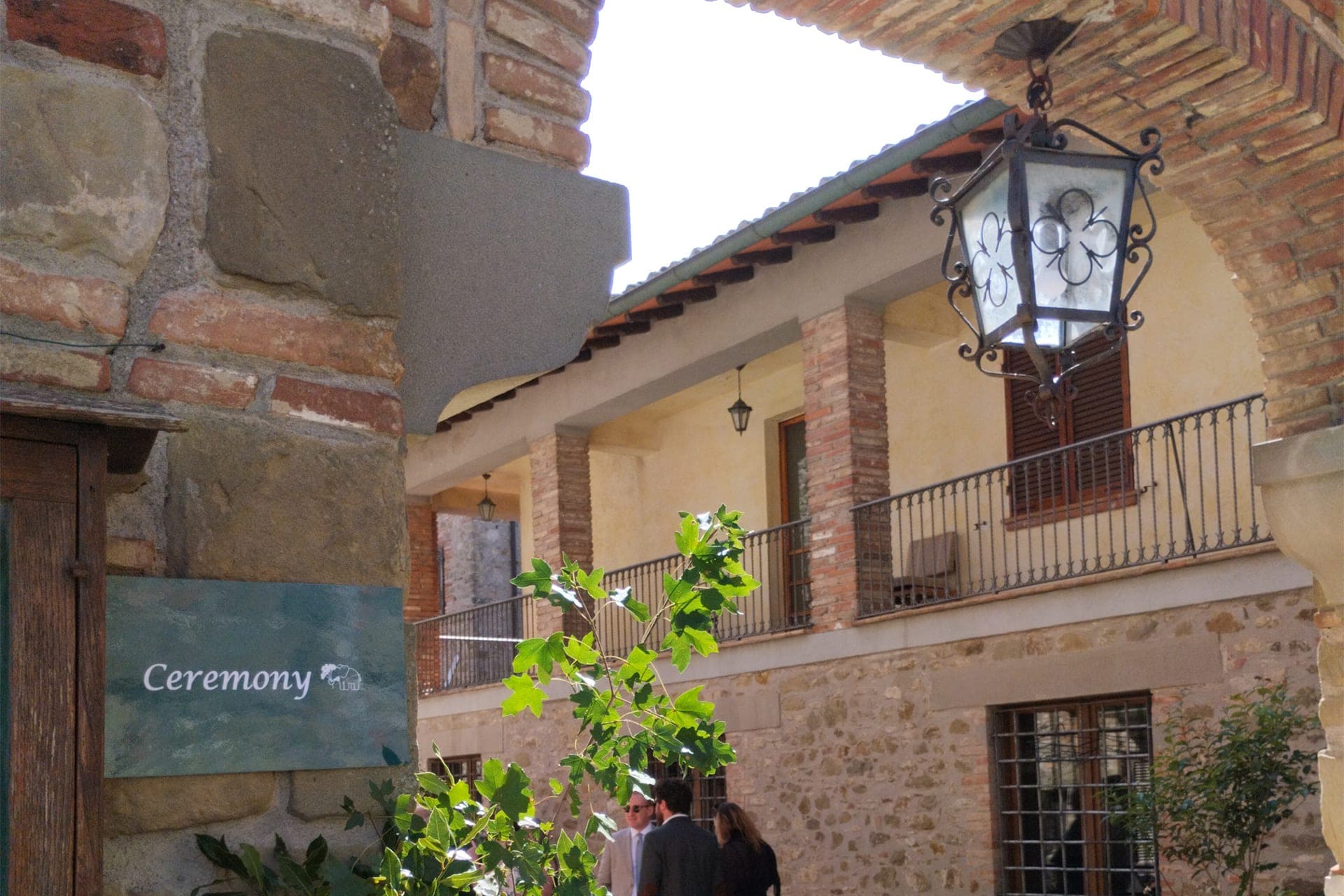 A sign that says Ceremony is mounted on a stone wall next to a courtyard with balconies.