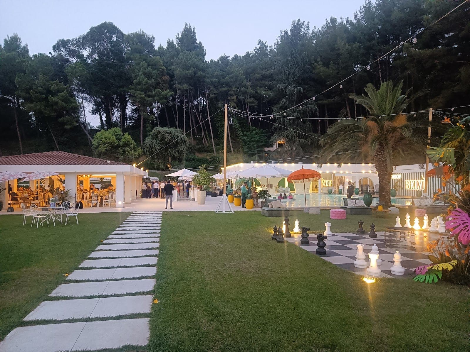A wedding venue with a pool, outdoor seating, and giant chess pieces on the lawn.