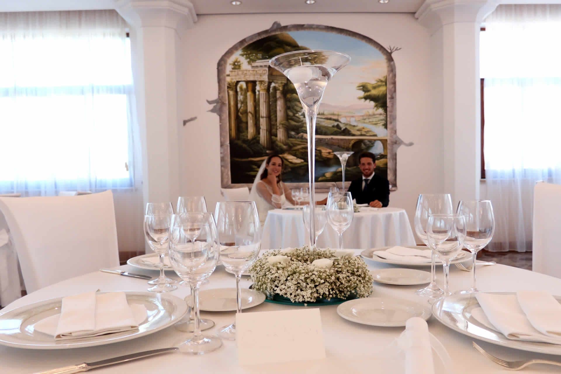A wedding reception table with place settings and a bride and groom in the background.