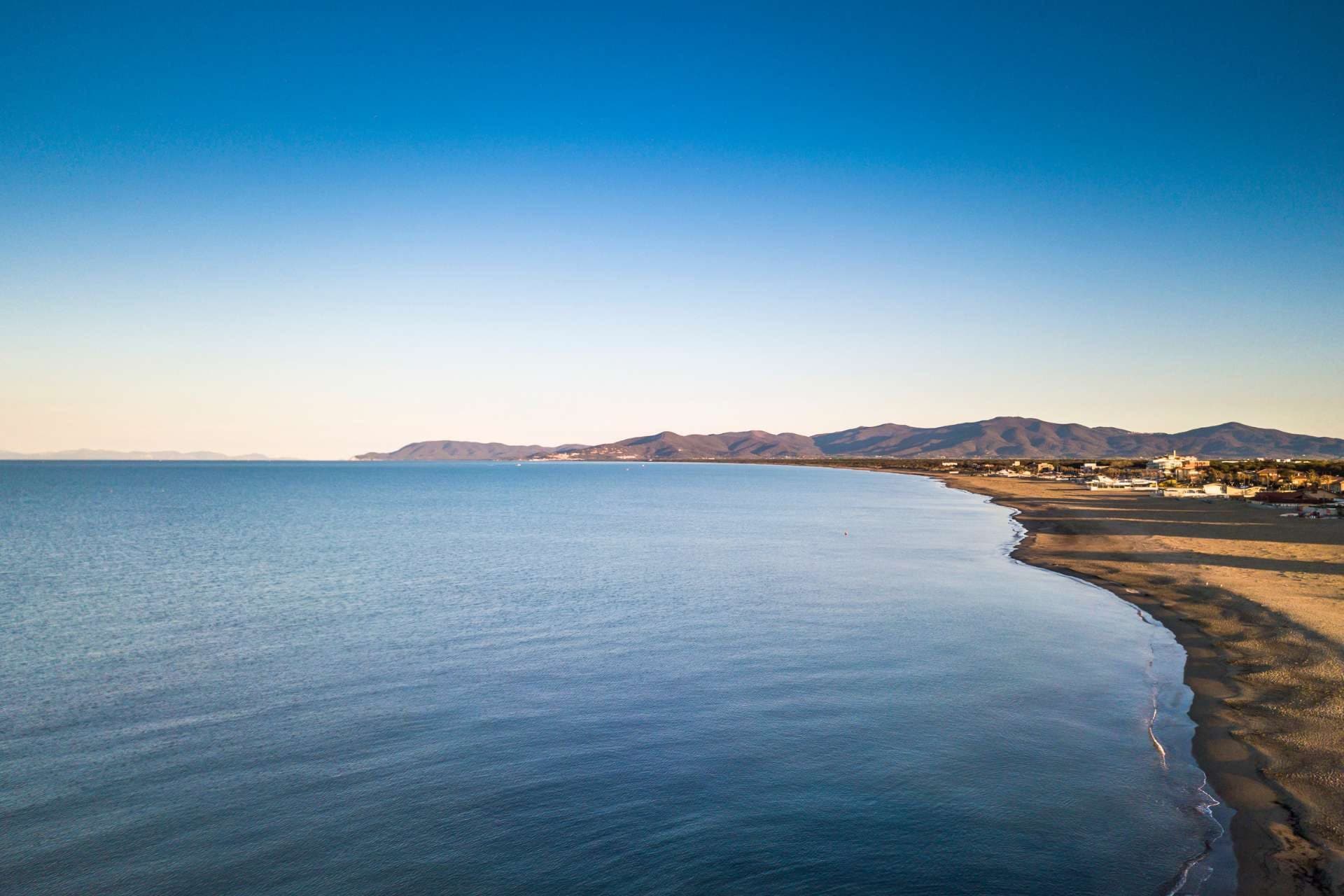 Aerial view of a coastline with calm blue sea and a sandy beach.