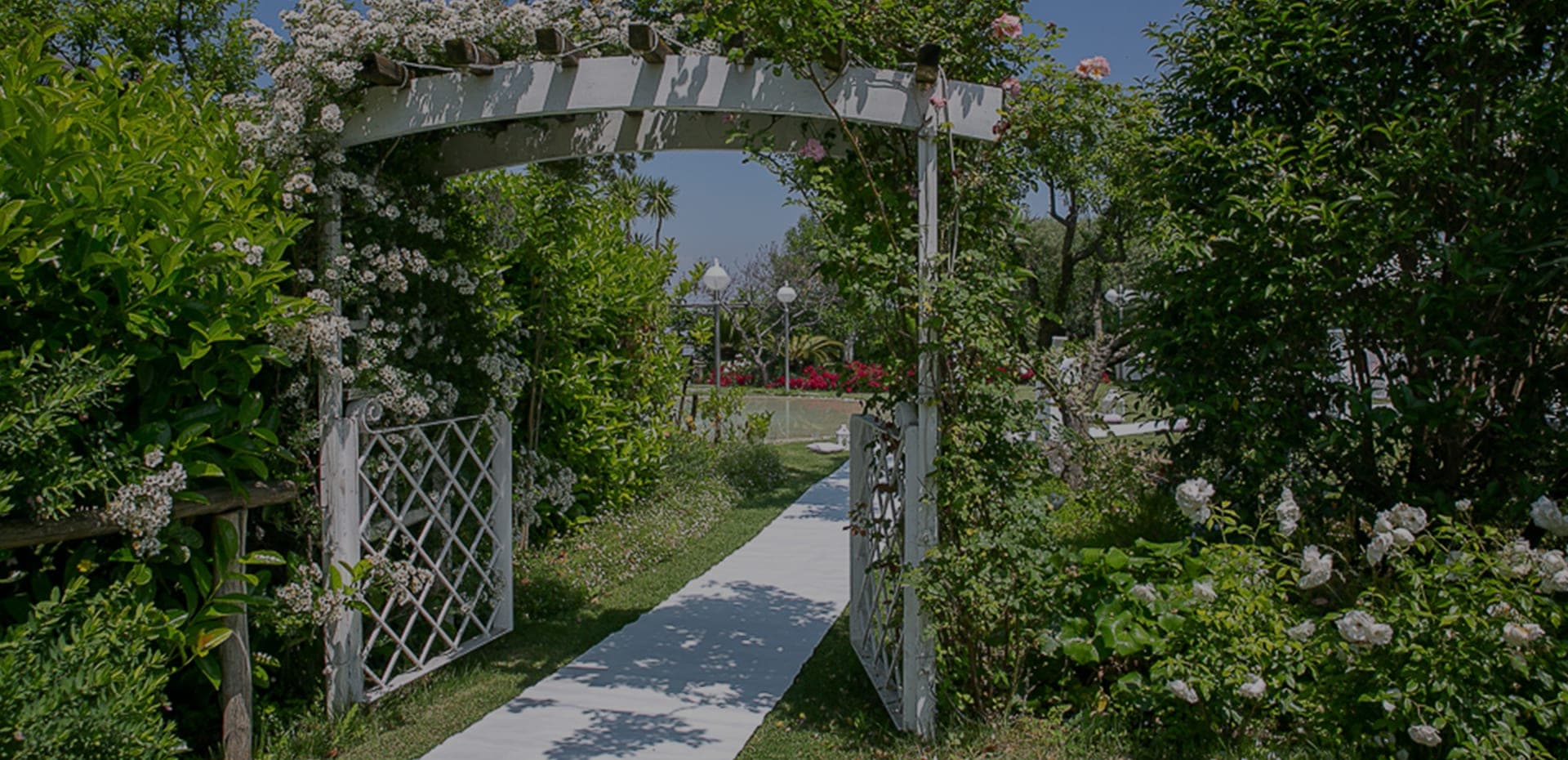 A garden path leads through a rose-covered archway towards a gazebo.