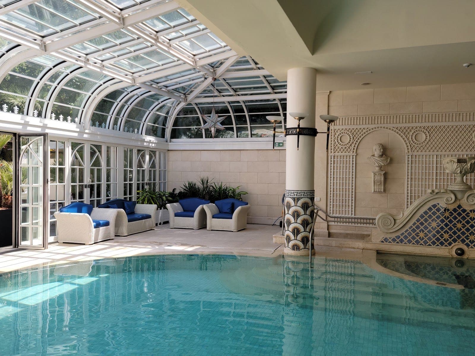 Indoor swimming pool with a glass roof and seating area.