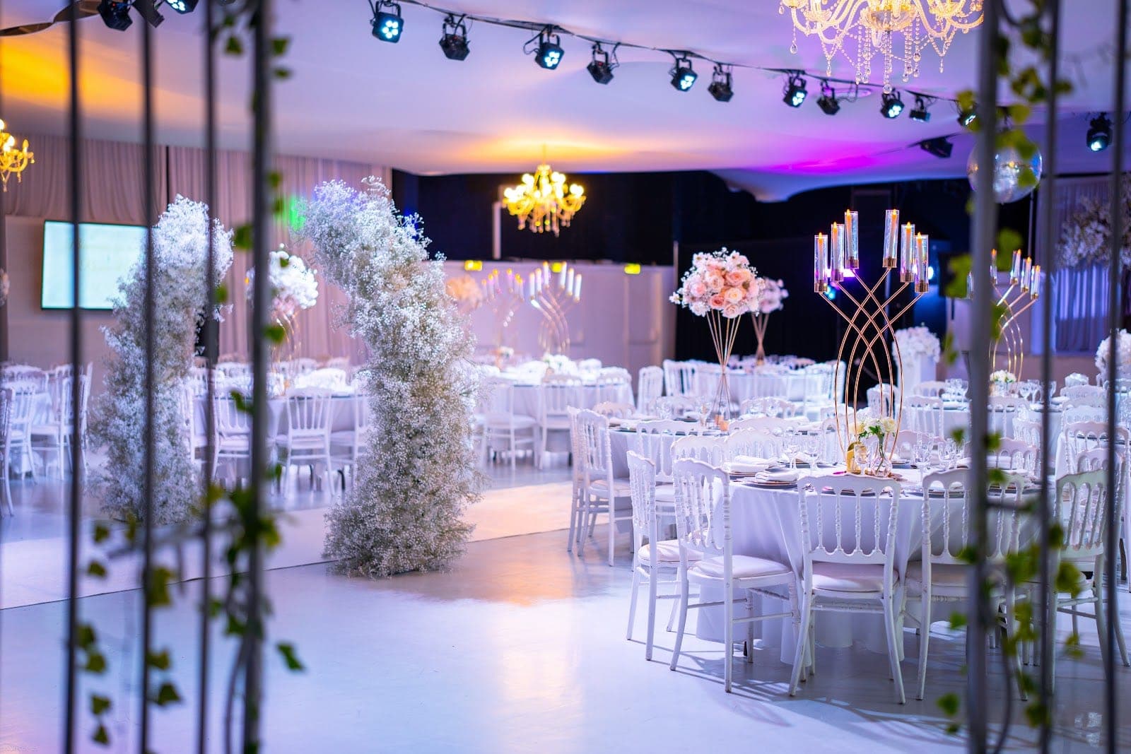 A wedding reception hall with white tables, chairs, and floral decorations.