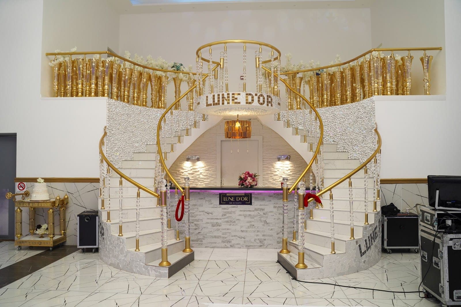 Grand staircase with gold railings and crystal accents, leading to a reception desk.