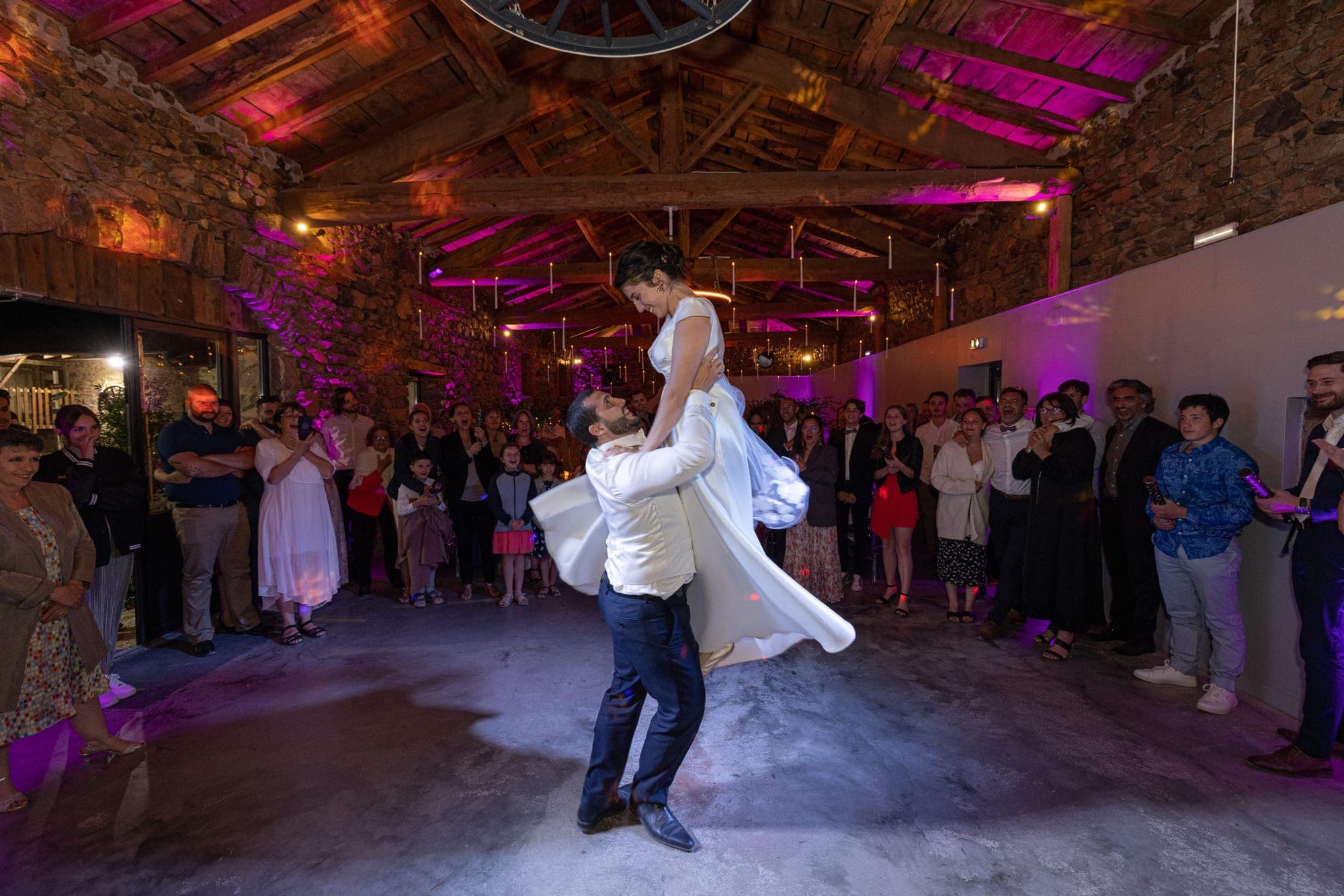 Bride and groom dancing in a rustic hall with guests watching.