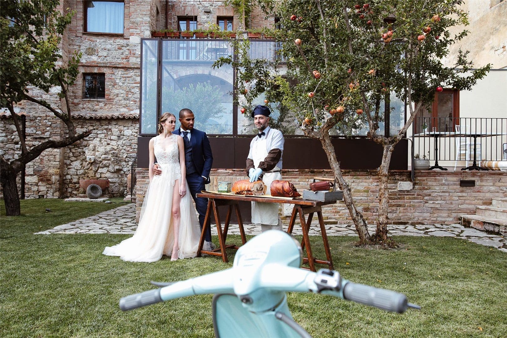 Wedding couple and chef in a courtyard with a scooter in the foreground.